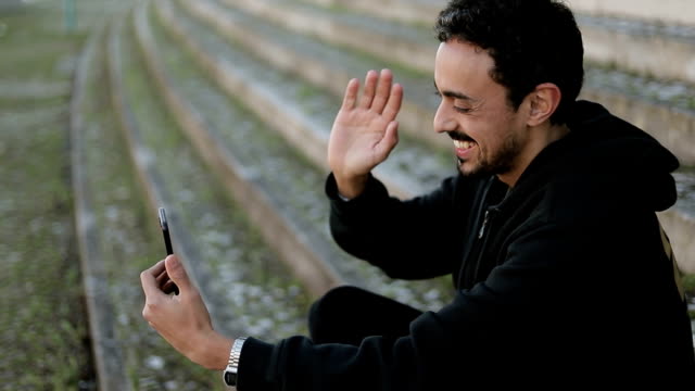Joven-árabe-hombre-teniendo-video-chat-fuera,-agitando-la-mano