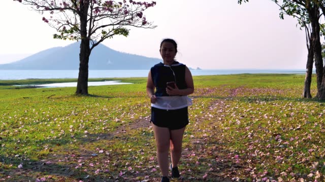 Eine-dicke-asiatische-Frau-joggt-abends-in-natürlichem-Sonnenlicht-und-hört-Musik.-Sie-versucht,-mit-Übung-Gewicht-zu-verlieren.--Konzept-Gesundheit-mit-Bewegung.-Zeitlupe