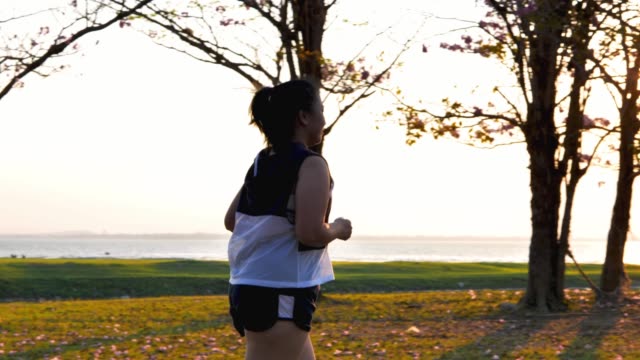 Eine-fette-asiatische-Frau,-die-abends-im-natürlichen-Sonnenlicht-joggt.
Sie-versucht,-mit-Übung-Gewicht-zu-verlieren.--Konzept-Gesundheit-mit-Bewegung.-Zeitlupe