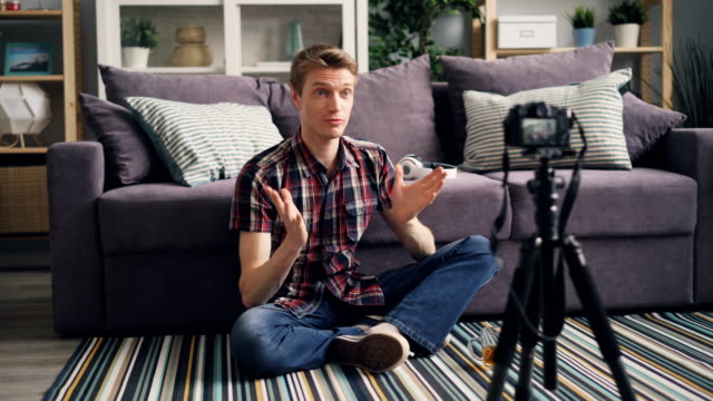 Junger-Mann-nimmt-Video-für-seinen-Online-Blog-auf-dem-Boden-zu-Hause-sitzen