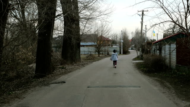 Sola-mujer-camina-a-lo-largo-de-la-carretera-entre-las-casas-y-los-árboles.