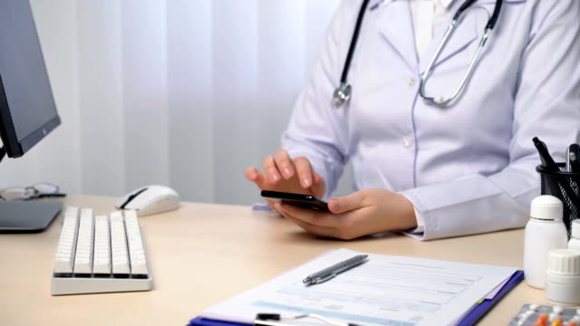Doctora-mujer-escribiendo-en-el-teléfono-inteligente,-enviando-mensajes-de-texto-a-un-paciente,-utilizando-aplicación-médica