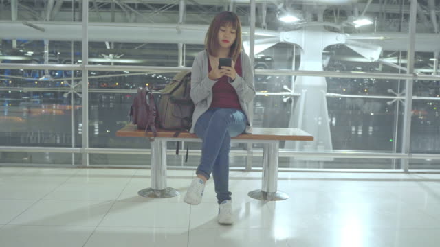 Mujer-asiática-usando-el-teléfono-inteligente-mientras-está-sentado-en-el-aeropuerto-internacional.