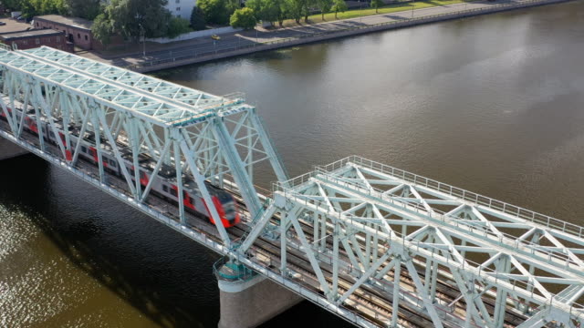 Aerial-view-of-the-railway-bridge,-with-a-moving-train-on-it,-across-the-river-flowing-through-a-major-city