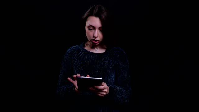 Nahaufnahme-Porträt-von-Erwachsenen-schöne-kaukasische-Brünette-weibliche-SMS-auf-dem-Tablet-mit-Hintergrund-isoliert-auf-schwarz