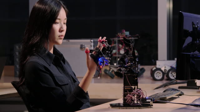 Asiatische-Frau-versuchen,-Roboter-Hand-im-Labor-zu-steuern.-Technologie--und-Innovationskonzept.