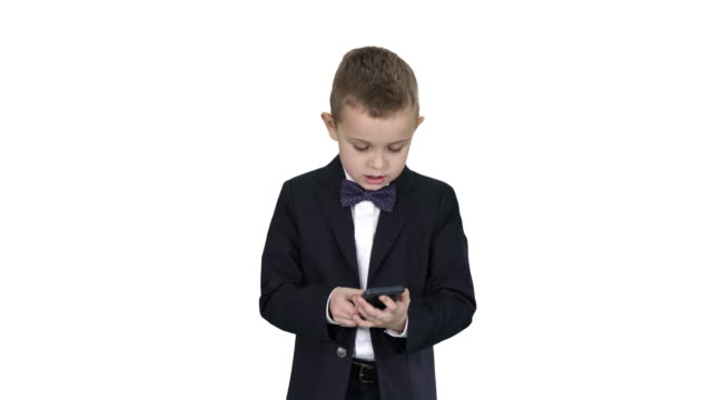 Niño-pequeño-en-traje-caminando-y-usando-el-teléfono-inteligente-sobre-fondo-blanco