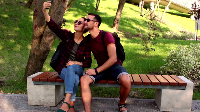 Una-joven-pareja-enamorada-es-fotografiada-sentada-en-un-banco-en-el-parque.-Sonríen-y-se-abrazan.