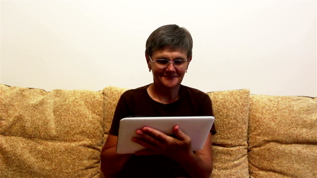 Atractiva-mujer-adulta-trabajando-en-su-tableta-mientras-está-sentada-en-un-sofá-en-casa.