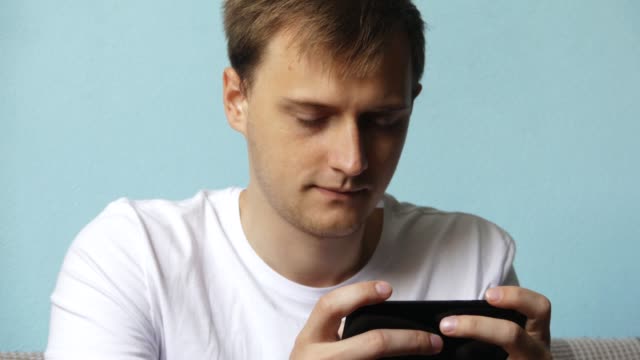 Hombre-serio-usando-un-teléfono-inteligente-jugando-juegos-o-escribiendo-un-mensaje,-sentado-en-el-sofá-en-la-sala-de-estar-durante-el-día-en-casa