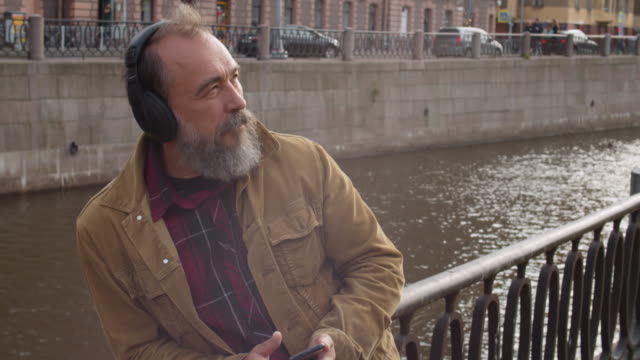 Senior-Man-Listening-to-Music-on-Embankment