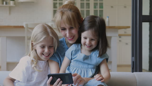 Glückliche-Mutter-und-kleine-Töchter-lachen-beobachten-Cartoons-auf-dem-Smartphone
