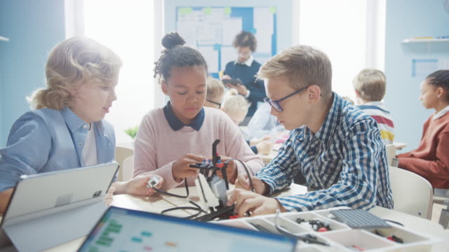 Elementary-School-Robotics-Classroom:-Diverse-Group-of-Brilliant-Children-with-Enthusiastic-Teacher-Building-and-Programming-Robot.-Kids-Learning-Software-Design-and-Creative-Robotics-Engineering
