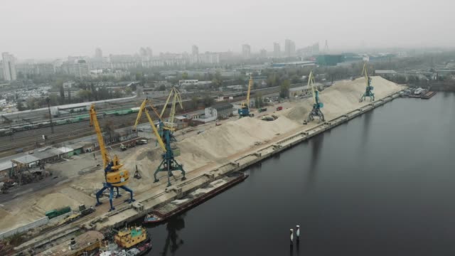Industrial-part-of-the-city-with-cargo-construction-cranes-and-old-cargo-railway-tracks.-Extraction-of-sand-from-barge-to-pile-of-sand-with-cargo-trucks