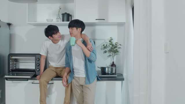 Asian-gay-couple-drinking-coffee,-having-a-great-time-at-home.-Young-handsome-LGBTQ+-men-talking-happy-relax-rest-together-spend-romantic-time-in-modern-kitchen-at-house-in-the-morning-concept.