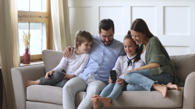 Padres-felices-con-niños-se-relajan-en-el-sofá-usando-aplicaciones-para-teléfonos-inteligentes