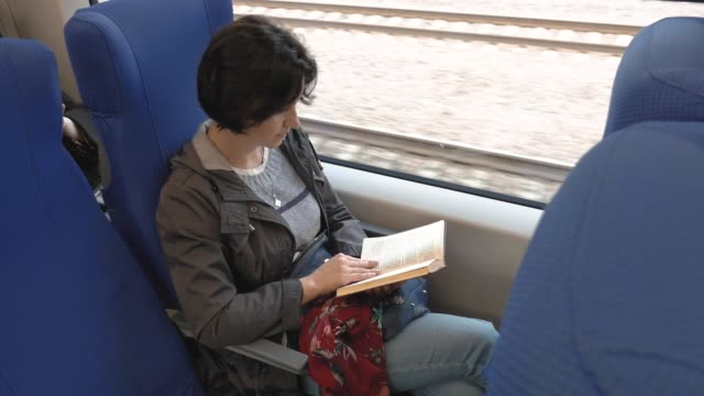 una-mujer-de-tamaño-mediano-se-sienta-en-un-tren.-Lee-un-libro.