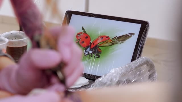 Close-up-of-a-tablet-with-a-picture-of-a-ladybug-on-a-table-in-a-tattoo-parlor.