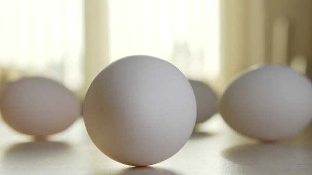 Cuatro-huevos-de-gallina-en-la-mesa-en-una-cocina-soleada,-un-huevo-se-gira