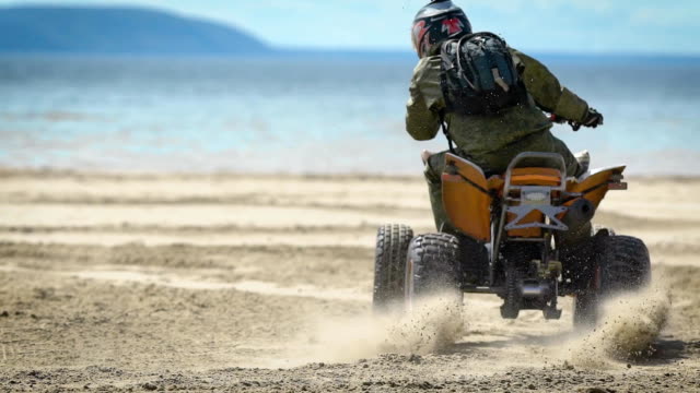 Strand.-Der-Mann-auf-dem-ATV.-Der-Racer-hat-Kreisverkehre-auf-Sand-auf-dem-ATV.-Die-Besonderheit-des-ATV-ist-riesige-Reifen,-hohe-Bodenfreiheit-und-hohe-Leistung