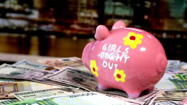 Pink-piggy-bank-on-rotating-surface-with-dollars-and-euro-banknotes.