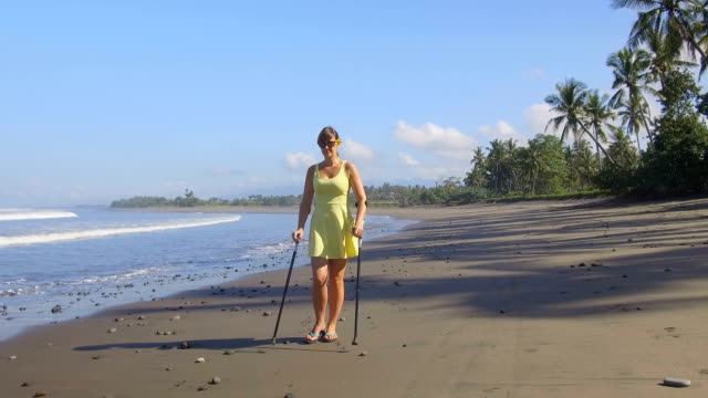 CLOSE-UP-Girl-with-crutches-walking-along-the-coastline-on-tropical-island-Bali