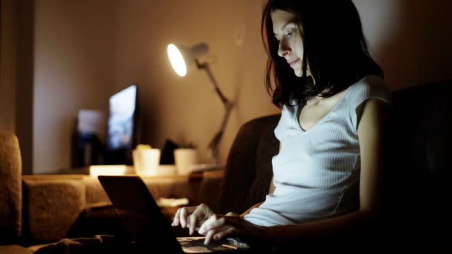 Young-concentrated-woman-using-laptop-computer-and-typing-message-at-home-in-night-time
