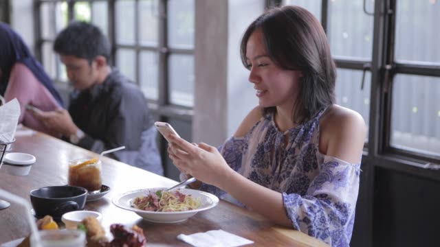 Mujer-está-comprobando-su-teléfono-mientras-comen-almuerzo-con-amigos-en-el-restaurante
