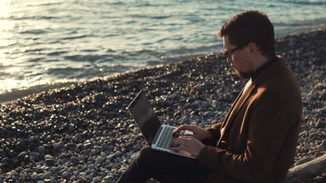 Geschäftsmann-arbeitet-abends-am-Meer-mit-Laptop-und-internet