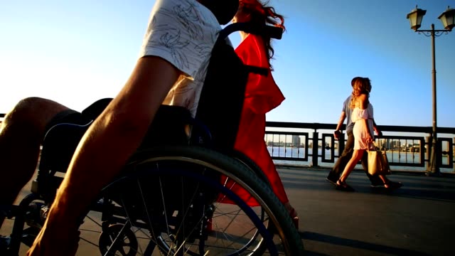 Guy-Fahrten-mit-Rollstuhl-und-ein-schönes-Mädchen-geht-mit-ihm-am-Meer-bei-Sonnenuntergang