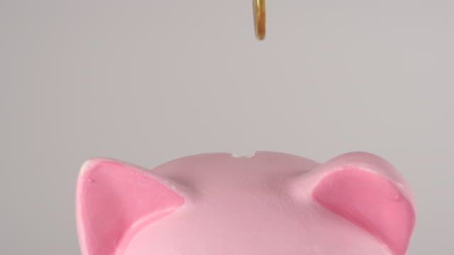 CLOSE-UP:-Männliche-Hand-wirft-goldene-Münze-in-ein-rosa-Schweinchen-sparschweinchen