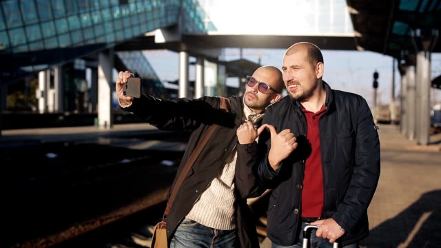 Dos-hombres-en-la-plataforma-del-ferrocarril-estación-esperando-la-llegada-del-tren-y-toman-fotos-selfie-en-un-smartphone.