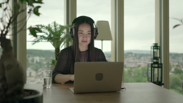 Young-Asian-woman-typing-on-laptop-while-listening-to-music-over-headphones