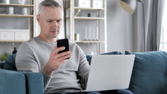 Graue-Haare-Mann-mit-Smartphone-und-Laptop-für-die-Arbeit