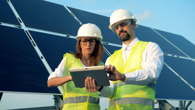 Two-workers-stand-near-solar-panels-with-a-tablet-close-up.