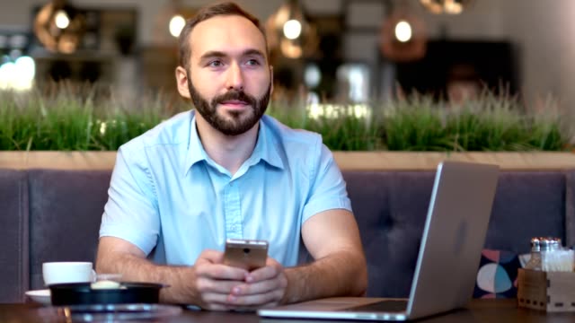 Porträt-des-lächelnden-jungen-Geschäftsmannes,-der-sich-über-Pause-Chats-mit-Smartphone-unterhält