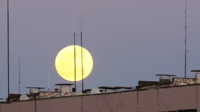 La-gran-luna-llena-sobre-el-tejado-de-un-edificio-Multistory-se-está-moviendo-hacia-arriba