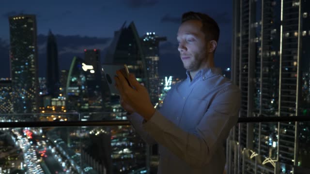 Hombre-joven-usando-la-tableta-para-hablar-y-comunicarse-con-el-fondo-de-la-vista-rascacielos