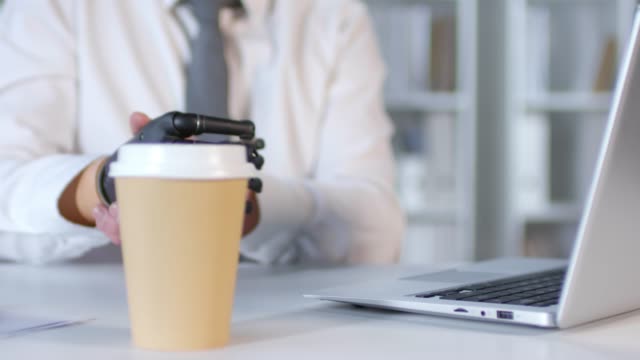 Geschäftsmann-mit-Prothesen-Arm-Typing-auf-Laptop-und-Trinkkaffee