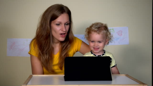 Young-woman-with-her-child-girl-looking-funny-cartoons-on-tablet-computer.