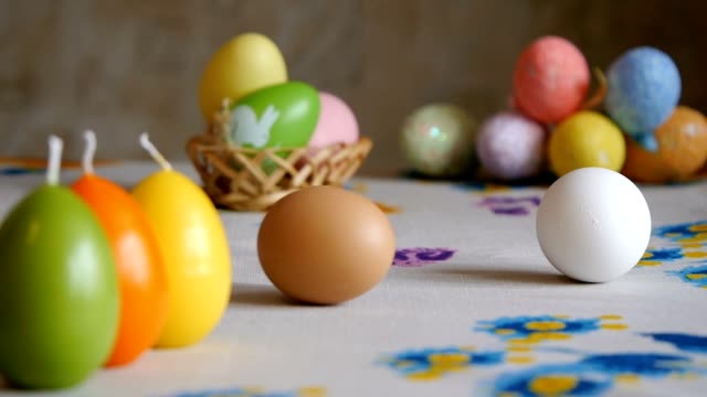 Happy-Easter.-female-hands-take-off-the-table-two-easter-eggs.-colorful-candles-and-colorful-Easter-eggs-in-the-background.