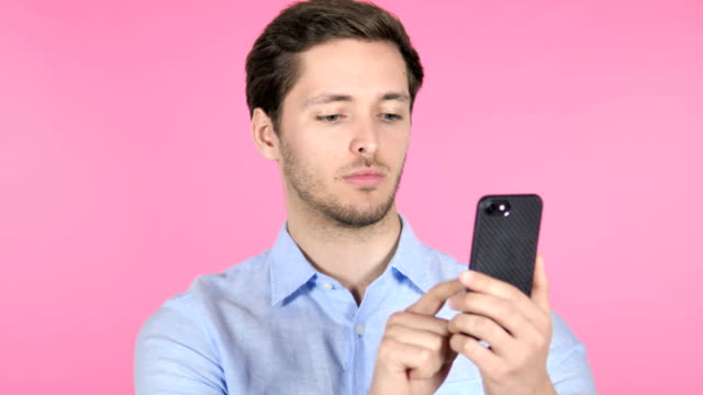 Junger-Mann-nutzt-Smartphone-auf-rosafarbenem-Hintergrund