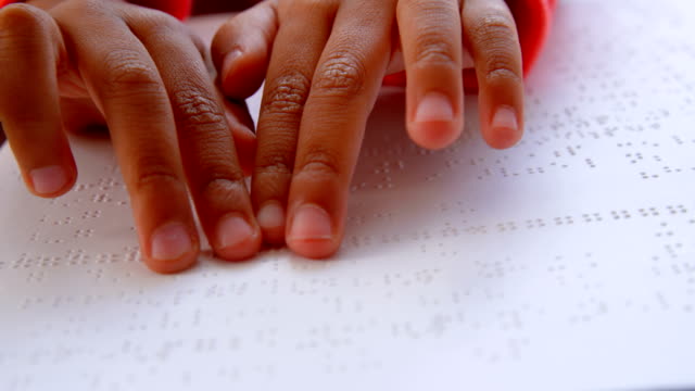 Close-up-of-blind-Asian-schoolboy-hand-reading-a-braille-book-in-classroom-at-school-4k