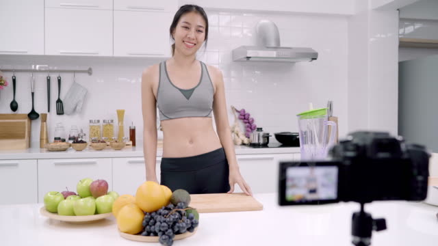 Blogger-sportliche-asiatische-Frau-mit-Kamera-Aufnahmen,-wie-man-Apfelsaft-Video-für-ihren-Abonnenten,-weiblich-verwenden-Bio-Obst-Apfelsaft-selbst-zu-Hause.-Gesundes-Lebensmittelkonzept.