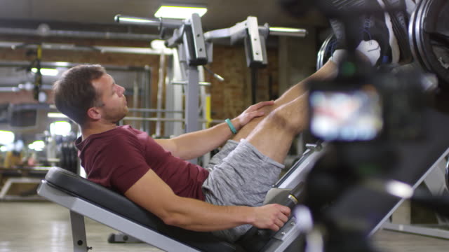 Fitness-Trainer-Lying-on-Leg-Press-Machine-and-Speaking-on-Camera