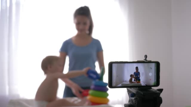 motherhood-blog,-young-mom-blogger-with-child-plays-developing-toys-while-recording-training-video-on-smartphone-for-subscribers-on-social-networks-in-streaming-live