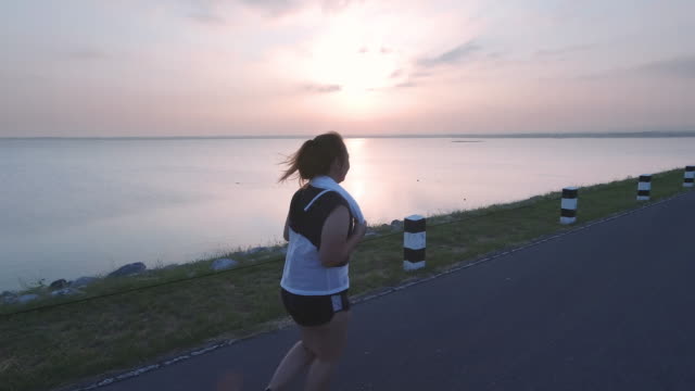 Asiatische-Frauen-joggen-in-der-Straße-am-frühen-Morgen-Sonnenlicht-am-Wasserspeicher-Pa-Sak-Jolasid-Dam.-Konzept-des-Gewichtsverlustes-mit-Bewegung-für-die-Gesundheit.-zeitlupe