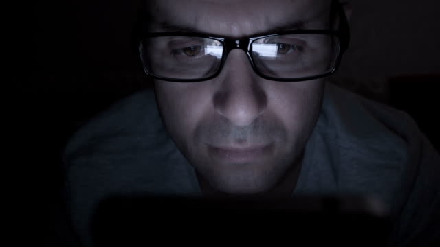 Close-up-of-man-with-glasses-using-smartphone.-Young-man-with-tablet-computer.-A-man-at-night-on-social-networks-using-a-smartphone.