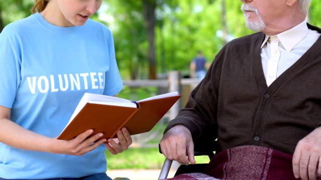 Aufrichtige-Sozialarbeiter-in-Lesebuch-für-behinderte-Rentner-in-Park,-Freiwilligenarbeit
