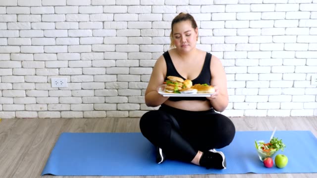 Übergewichtige-junge-Frau-in-Sportbekleidung,-die-nach-dem-Training-salatstatt-Hamburger-wählt